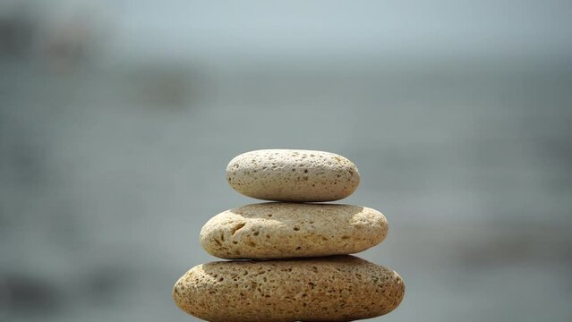 Woman bilds stones pyramid on the seashore on a sunny day on the blue sea background. Happy holidays. Pebble beach, calm sea, travel destination. Concept of happy vacation on the sea, meditation, spa