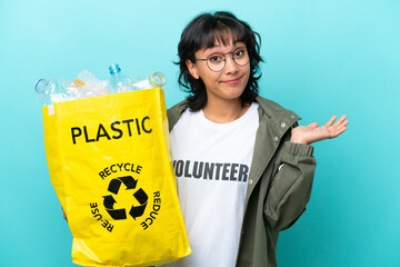 Young Argentinian woman holding a bag full of plastic bottles to recycle isolated on blue...