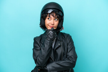 Young Argentinian woman with a motorcycle helmet isolated on blue background having doubts