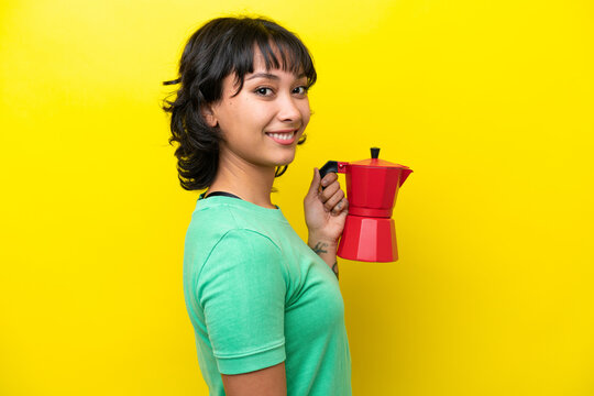 Young Argentinian Woman Holding Coffee Pot Isolated On Yellow Background Smiling A Lot