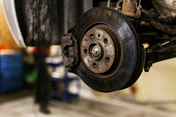 A close-up of the brake caliper on an old car that is lifted on an electric lift in a workshop.
