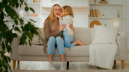 Caucasian family at living room. Woman mother babysitter listen secret from little daughter kid...