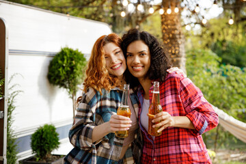 Portrait of two young women drinking drinks, hugging and smiling. Two girlfriends are relaxing in nature outside the city, enjoying the summer.