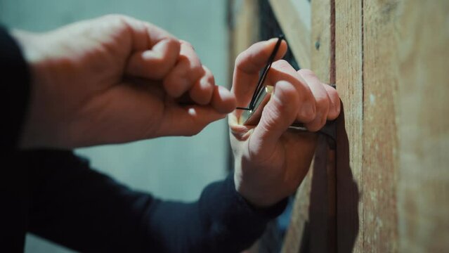 Man picking a lock on a storage cage door in a dimly lit warehouse. Crime. Burglary