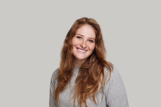 Lovely smiling woman with curly ginger hair and positive friendly smile looking at camera, studio portrait