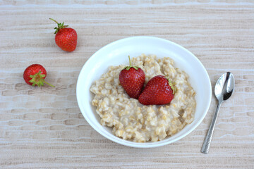 A bowl of oatmeal with strawberries on it with teaspoon isolated on beige background