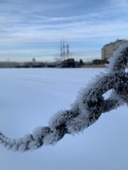 Large, large, heavy metal chain covered with frost. In the background, the ship and the Strelka of Vasilyevsky Island against the blue sky with clouds in St. Petersburg.
