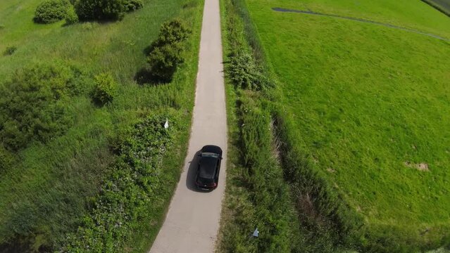 drone shot of a black car driving between fields on a small path
