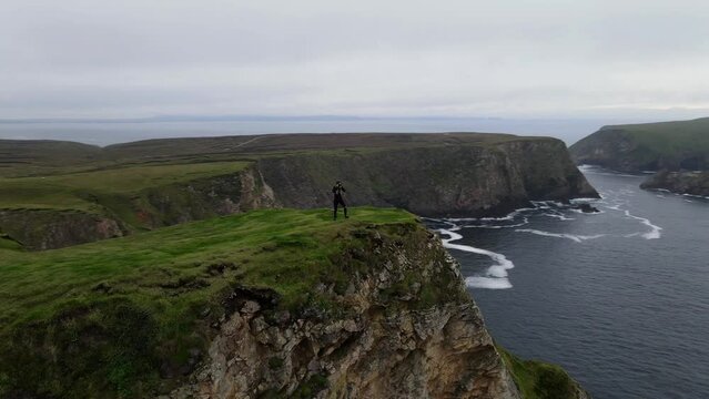 Female photographer and explorer on a cliff in Ireland in the middle of nowhere taking photos