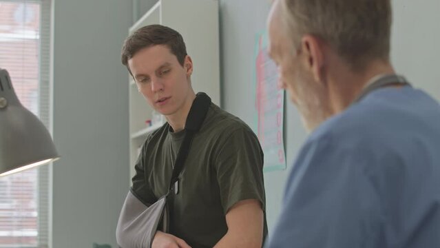 Medium shot of young Caucasian army officer with injured arm having medical appointment at doctor office