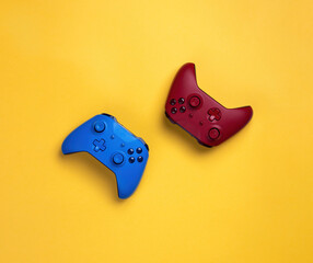Two wireless gamepads red and blue lie on a yellow background.  Confrontation of players, battle in the game online © Nyaaka