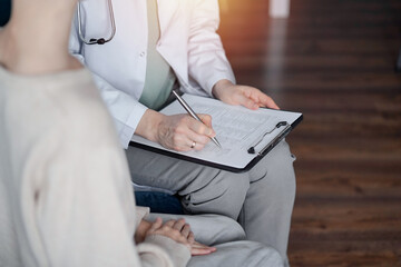 Doctor woman and kid boy patient at home medical exam. The pediatrician filling up medical form on clipboard, close up. Medicine, healthcare concepts
