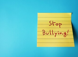 Yellow note stick on blue copy space background with handwritten text STOP BULLYING, stop hurting...