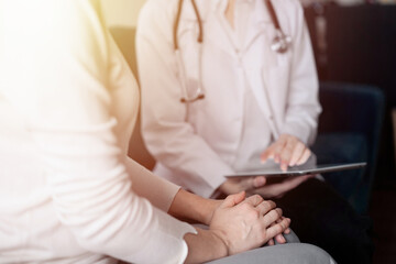 Doctor and patient sitting at sofa in clinic office. The focus is on female woman's hands, close up. Medicine concept
