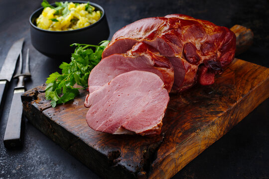 Traditionell geschmortes badisches Sch&auml;ufele mit Kartoffelsalat und Petersilie aufgeschnitten als close-up auf einem rustikalen Holz Schneidebrett 