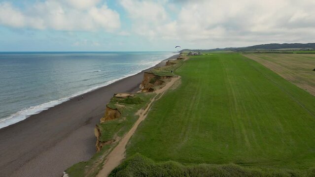 Aerial view of a powered parachute flying over the grass field near the sea