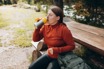 Happy redhead Woman in active trekking clothes having a halt after hiking. Hiker drinking water...