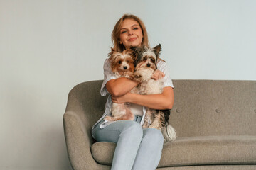 Holding and embracing the animals. Woman is sitting on a sofa with two cute dogs