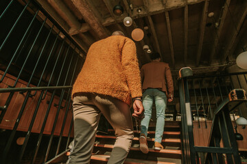 Back view photo of two male multiracial business partners walking upstairs at the coffee bar