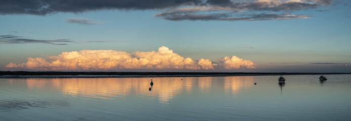 Magnifique nuage cumulus ou cumulonimbus au coucher du soleil reflété dans l'estuaire de la Seudre en Charente Maritime, au loin deux bateaux de pêche amarrés sur leurs bouées.	