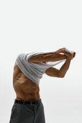 Portrait of muscular male fashion model taking off t-shirt isolated over white studio background. Masculinity