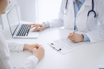 Doctor and patient discussing something and using laptop while sitting opposite each other at the desk in clinic office. Perfect medical service and medicine concept