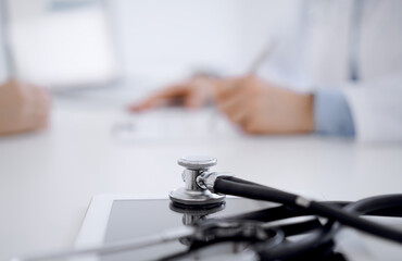 Stethoscope lying on the tablet computer in front of a doctor and patient sitting opposite each other at the background . Medicine, healthcare concept