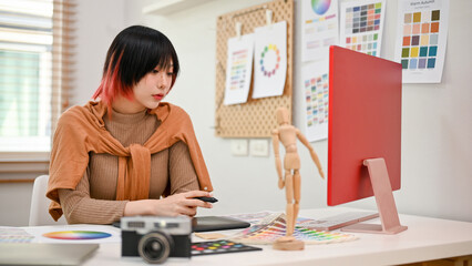 Attractive Asian female graphic designer working on her project in the office.