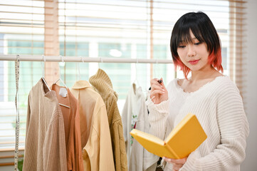 Charming Asian female fashion clothes shop owner checking her product stock