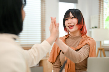 Obraz premium Cheerful Asian female worker giving high five to her colleague while working together