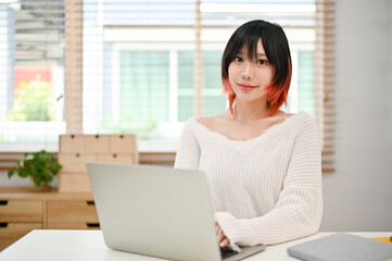 Attractive Asian female using her laptop at her home workspace.