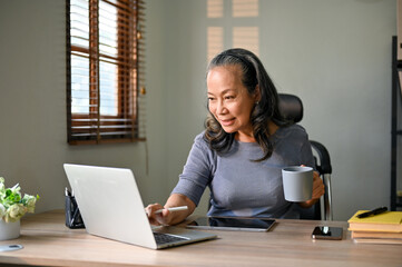 Professional Asian-aged businesswoman working on her business tasks on laptop