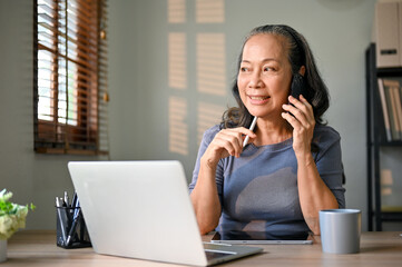 Successful Asian-aged businesswoman is talking on the phone with her business partner