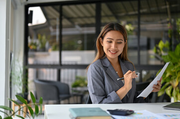 Obraz premium Attractive Asian businesswoman analyzing financial data on reports and working at her desk.