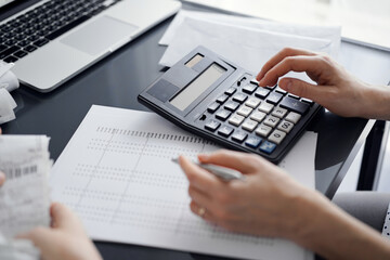 Woman accountant using a calculator and laptop computer while counting taxes for a client. Business audit and finance concepts