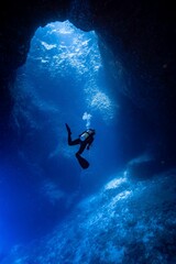 Vertical shot of a scuba diver swimming in an underwater cave near to the surface