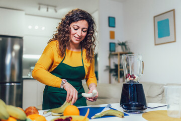 Beautiful, happy young woman in casual home clothes prepares fitness cocktails with different seasonal fruits.