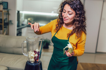 Beautiful, happy young woman in casual home clothes prepares fitness cocktails with different seasonal fruits.