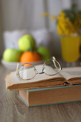 Cup of tea, plates with cookies, glass of orange juice, books, reading glasses, bowl of fruit and candles on the table. Selective focus.