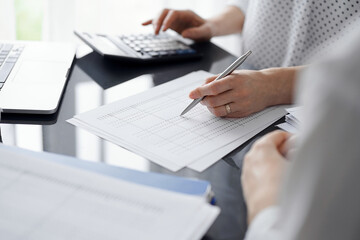 Woman accountant using a calculator and laptop computer while counting taxes for a client. Business...