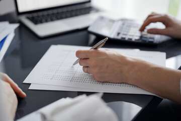 Woman accountant using a calculator and laptop computer while counting taxes for a client. Business audit and finance concepts