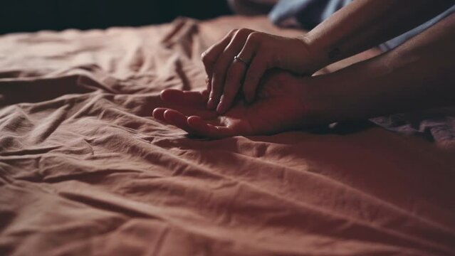 Closeup of couple hands caressing on bed