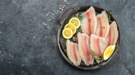 Raw tilapia fish fillet sliced for steak with lemon and spices on a dark background. Long banner format. top view