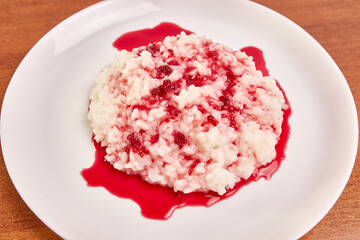Rice porridge covered with raspberry jam on a white plate.