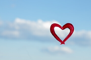 Red Heart on the window on the background of the sky on a sunny day. A symbol of love and pease