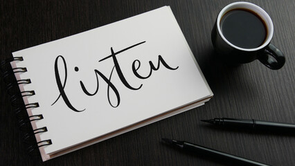 LISTEN black hand lettering in notebook with cup of espresso and pens on black wooden desk