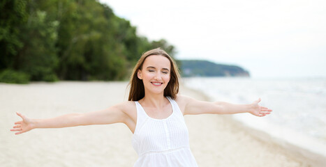 Fototapeta na wymiar Happy smiling woman in free happiness bliss on ocean beach standing with open hands. Portrait of a multicultural female model in white summer dress enjoying nature