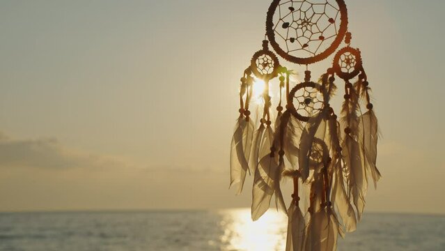 Dreamcatcher golden disk sun slow motion close up on background of blue sea sky in rays of sun at dawn in summer. Silhouette Indian talisman symbol. Boho style