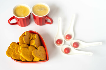 Coffee in red mugs with heart shaped gingerbread cookies in a red ceramic heart shaped pot, and red chocolate pralines.