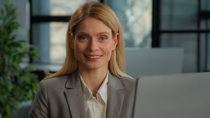 Close up Caucasian middle-aged woman employee in office with computer working online. Executive businesswoman smiling to camera with laptop at workplace Happy corporate business portrait manager smile